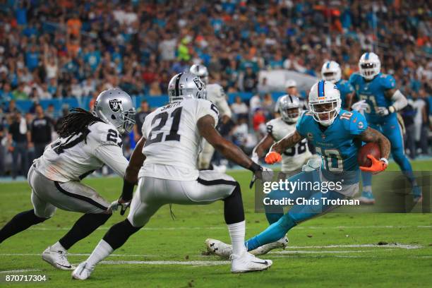 Wide receiver Kenny Stills of the Miami Dolphins is challenged by free safety Reggie Nelson of the Oakland Raiders and cornerback Sean Smith of the...