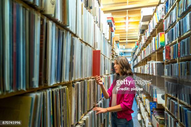 young female music fan searching  in large vinyl record collection, wide shot - record shop stock pictures, royalty-free photos & images