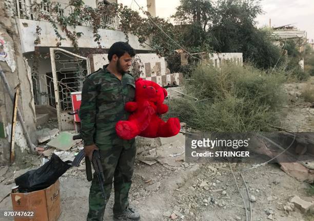 Member of the Syrian government forces carries a teddy bear in a northeastern district of Deir Ezzor on November 5 after troops retook the city from...