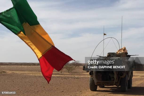 Soldiers of the France's Barkhane mission patrol in a military vehicle next to a Malian national flag on November 2, 2017 in central Mali, in the...
