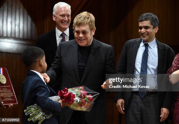 Founder Elton John is presented with flowers from Chase Sullivan after receiving the Harvard Foundation's Peter J. Gomes Humanitarian of the Year...