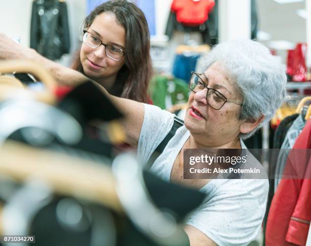 the silver-haired 65-years-old active senior woman and her teenager granddaughter shopping in the clothing retail store - 13 years old imagens e fotografias de stock