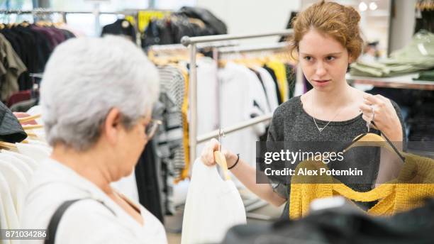 the silver-haired 65-years-old active senior woman and her teenager granddaughter shopping in the clothing retail store - 14 15 years girl stock pictures, royalty-free photos & images