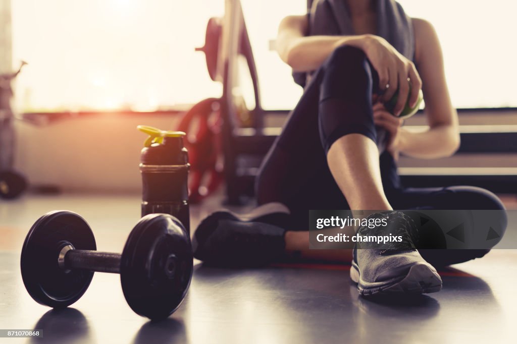 Allenamento di allenamento femminile in palestra fitness rottura rilassarsi tenendo frutta di mele dopo l'allenamento sport con manubrio e protein shake bottiglia sano stile di vita bodybuilding.