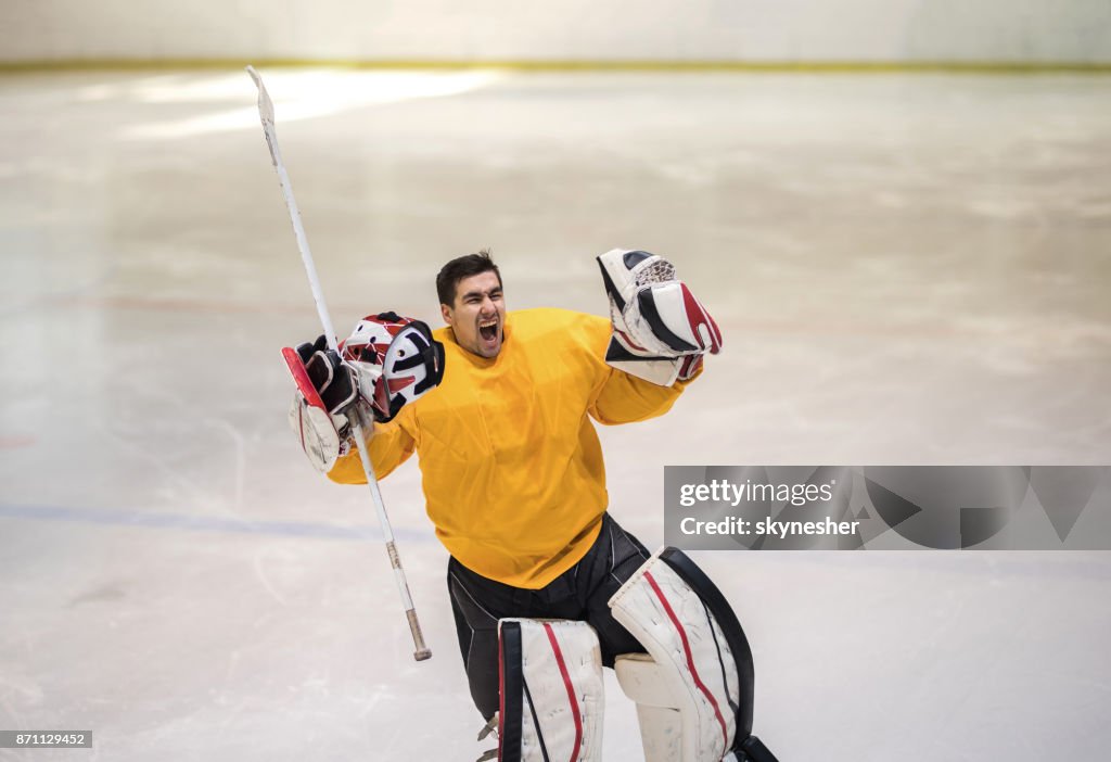 Young ice hockey goalie celebrating the victory in a rink and shouting of joy.