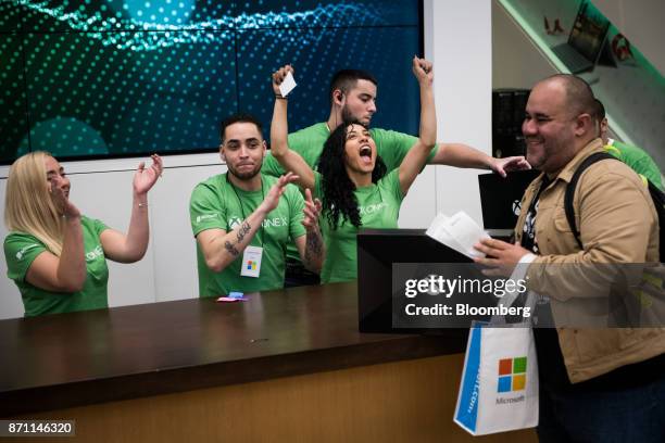 Employees cheer for a customer as he purchases an Xbox One X game console during the Microsoft Corp. Global launch event in New York, U.S., on...