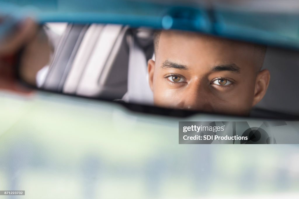 Closeup of young man's reflection in rear view mirror