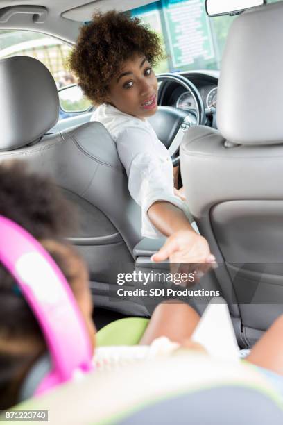 young mother reaches toward daughter in back seat of car - distracted driving stock pictures, royalty-free photos & images