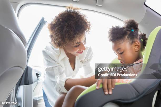 young mother buckles preschooler into car seat - kid car safety stock pictures, royalty-free photos & images
