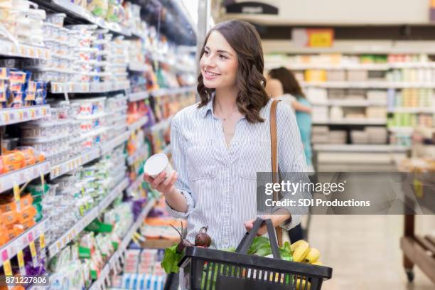 happy young woman shops in dairy section of grocery store - women yogurt stock pictures, royalty-free photos & images