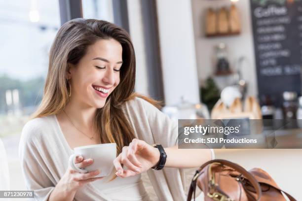 mujer joven alegre comprueba el tiempo durante la pausa café - célula cultivada fotografías e imágenes de stock