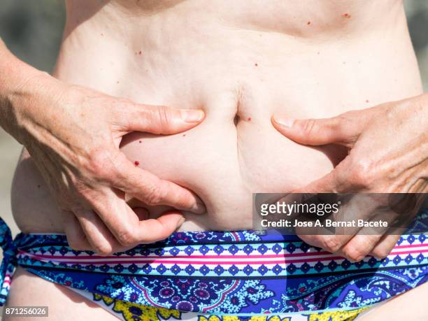 a close-up image of a woman mature with  belly fat pinching itself, white-skinned, with bikini in the light of the sun in the beach - fat woman stock-fotos und bilder