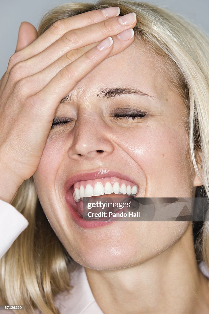 Woman laughing with hand on forehead, close-up