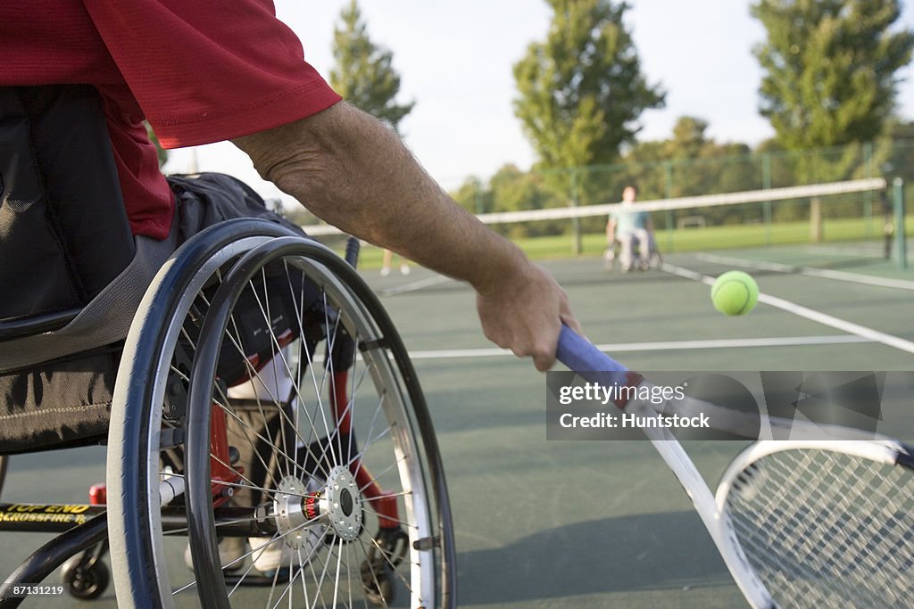 Low section view of a man sitting in a wheelchair and playing tennis.