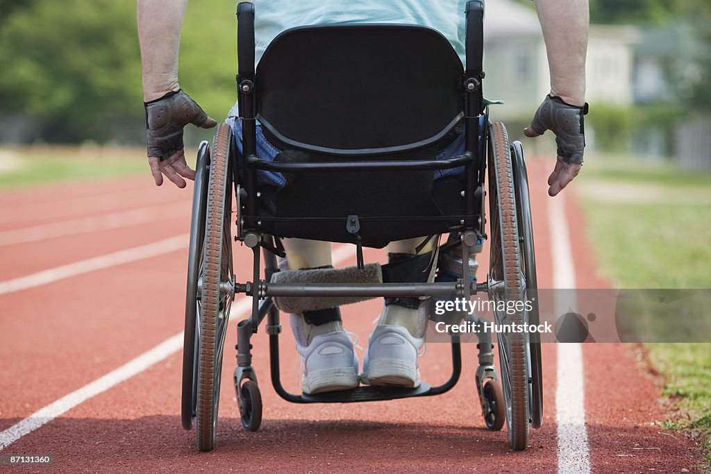 Rear view of a man sitting on a wheel chair on a race track