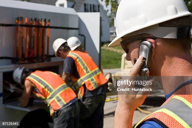 construction worker talking on mobile phone, two men at truck in background - bending stock pictures, royalty-free photos & images