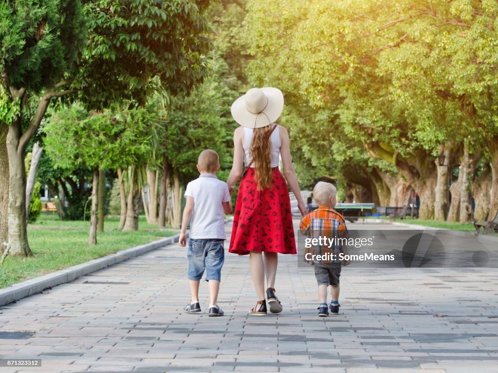 Mum and two sons walking in the park, sunny day. View from the back