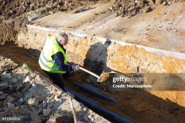 worker works with shovel in a trench on pipeline construction site - trench town stock pictures, royalty-free photos & images