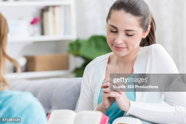 mujer joven ora con amigo en la casa estudio de la biblia - religious text fotografías e imágenes de stock