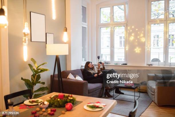 couple taking selfie with smartphone on sofa at home during christmas - couple lit stock pictures, royalty-free photos & images