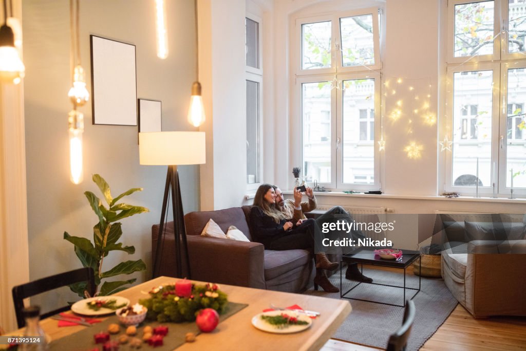 Casal tendo selfie com smartphone no sofá em casa durante o Natal