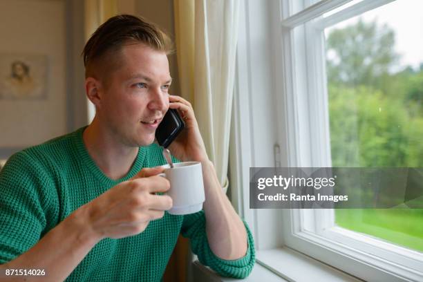 hübscher junger mann am fenster zu hause entspannen - turku stock-fotos und bilder