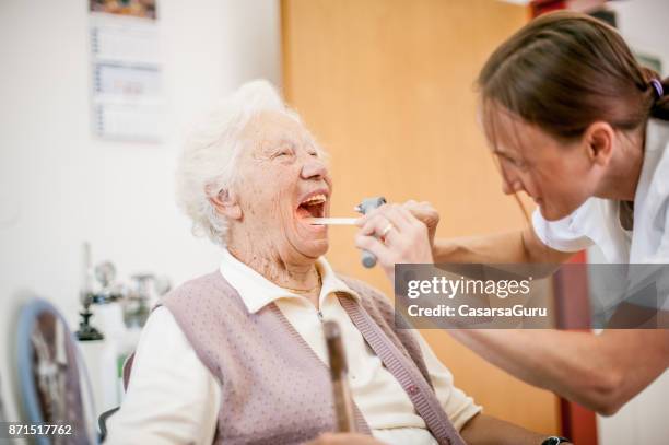 female doctor examining throat of senior woman in rest home - tongue depressor stock pictures, royalty-free photos & images