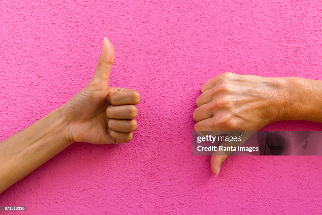 Two hands giving thumbs up and thumbs down against pink background