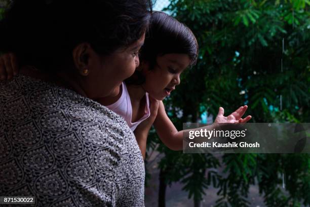 woman and infant enjoying rain in outdoor with a green backdrop - daily life in kolkata stock pictures, royalty-free photos & images