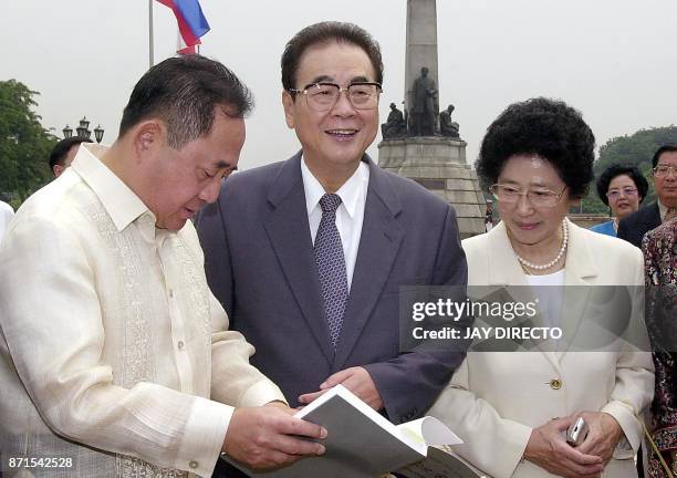 Chinese number two leader Li Peng smiles beside his wife Zhu Lin , while Philippine House Speaker Jose de Venecia shows him a book about Jose Rizal,...