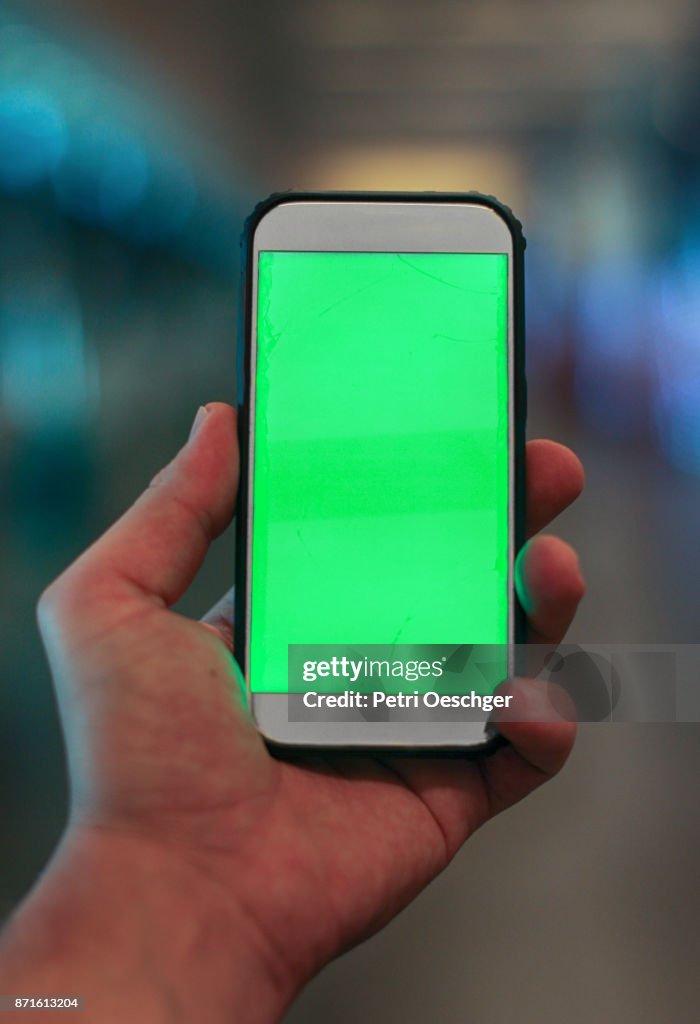 A Young man holding a green screen smartphone at Cape Town International Airport.
