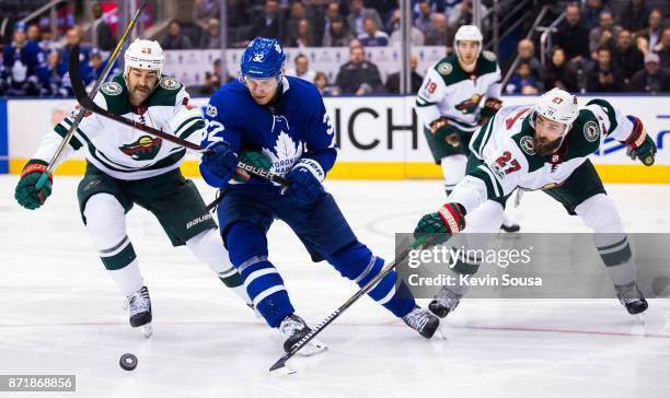 Daniel Winnik of the Minnesota Wild, Josh Leivo of the Toronto Maple Leafs and Kyle Quincey of the Minnesota Wild battle for the puck during the...