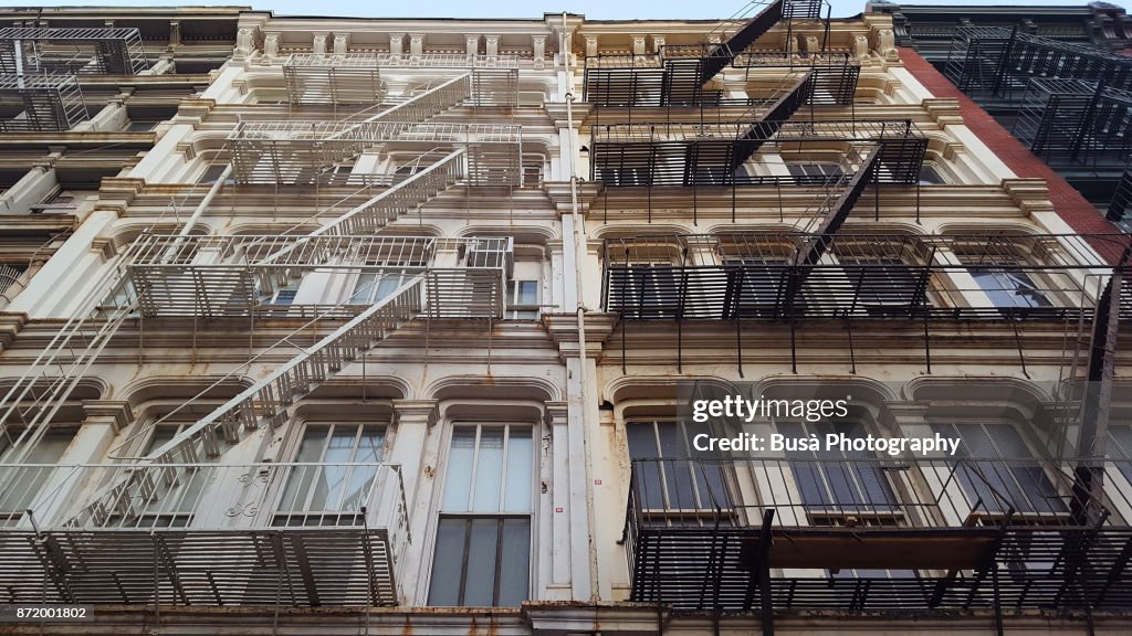 View from below of typical cast iron buildings with fire escapes along Greene Street in Soho, New York City
