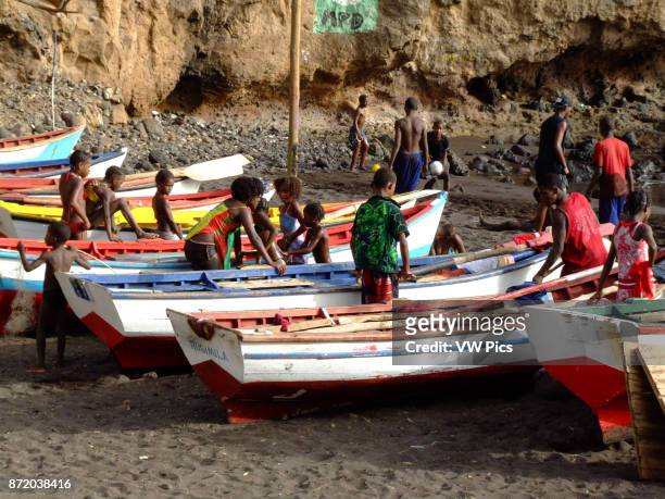 Children play on colorful fishing boats on shore in Cidade Velha on the island of Santiago, Cabo Verde or Cape Verde.