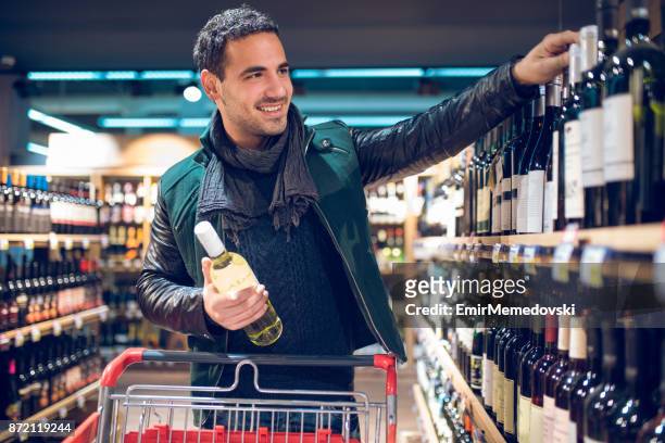 young man in a supermarket choosing wine - buying alcohol stock pictures, royalty-free photos & images