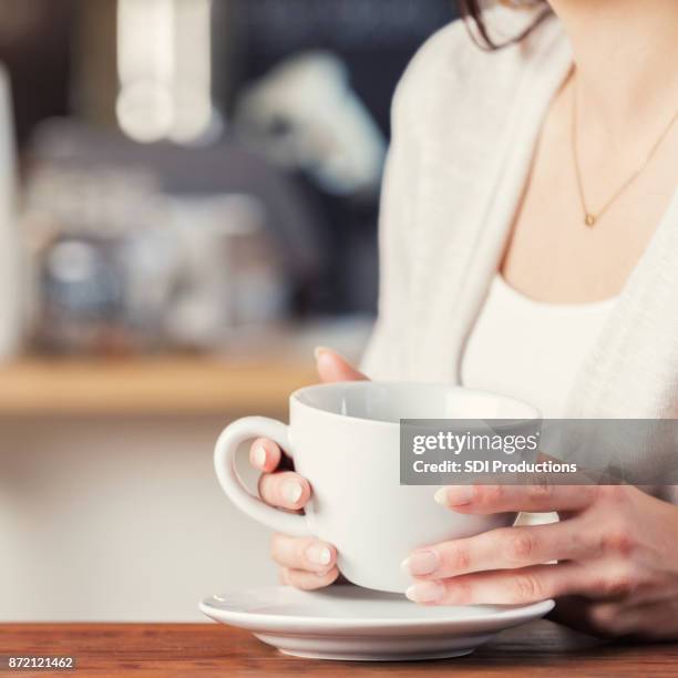 nicht erkennbare sitzende frau hält kaffeetasse über untertasse - untertasse stock-fotos und bilder