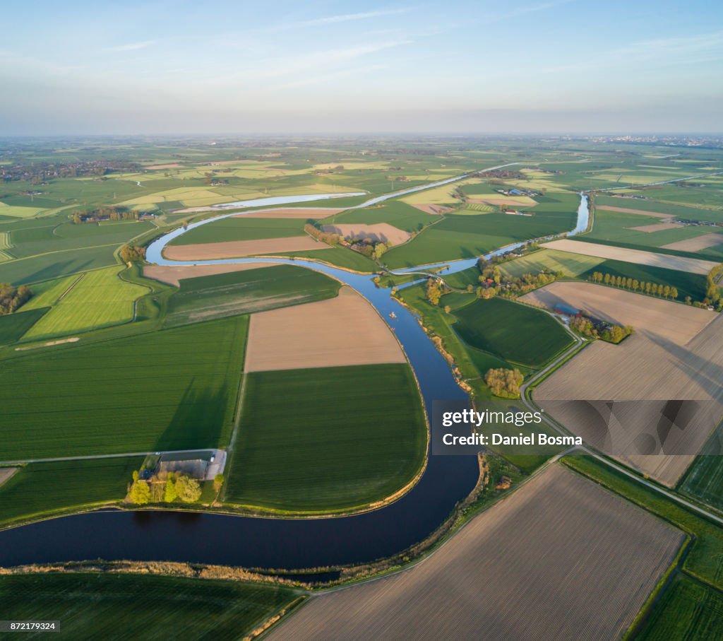 Natural curves of a river surrounded by a cultivated Dutch landscape, seen from the air