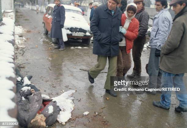 People walk past a dead man lying in the street in Bucharest during the Romanian Revolution, December 1989.