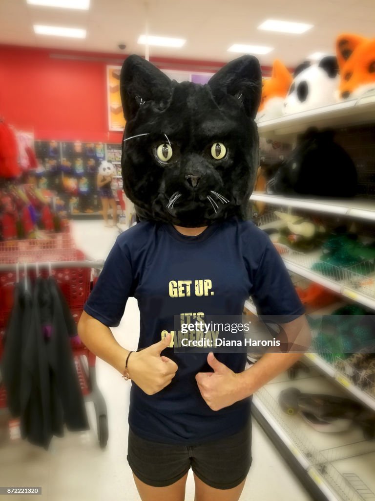 A girl is standing in a store wearing a funny black cat mask