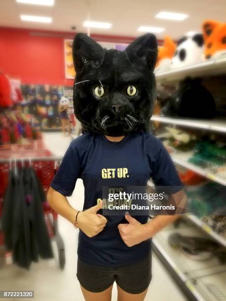 A girl is standing in a store wearing a funny black cat mask