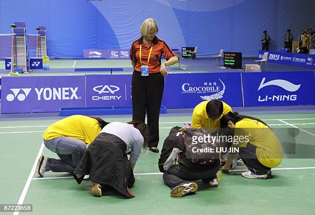 An official looks at her watch as volunteers repair the line on the court before the preliminary match between Malaysia and Denmark at the Sudirman...