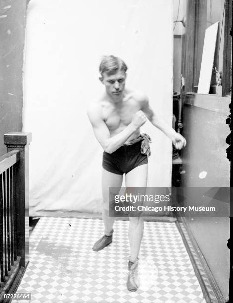 Full-length portrait of Battling Nelson, lightweight boxing champ, standing upright in boxing stance, facing the camera in a stairwell hallway at the...