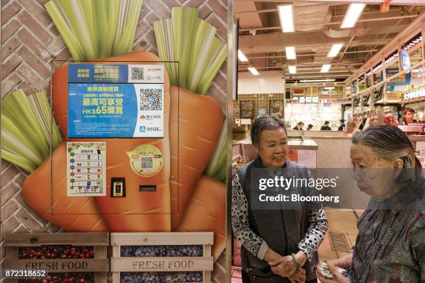 Elderly women stand next to a screen displaying an advertisement for Ant Financial Services Group's Alipay, an affiliate of Alibaba Group Holding...