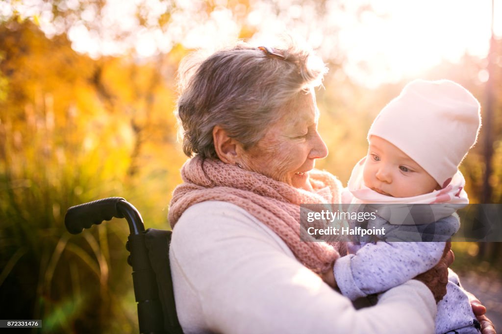 Eine ältere Frau im Rollstuhl mit Baby im Herbst Natur.