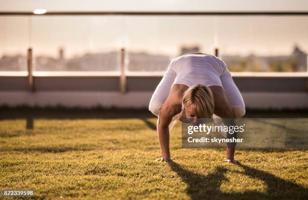young woman practicing yoga in bakasana pose on a terrace. - crow pose stock pictures, royalty-free photos & images