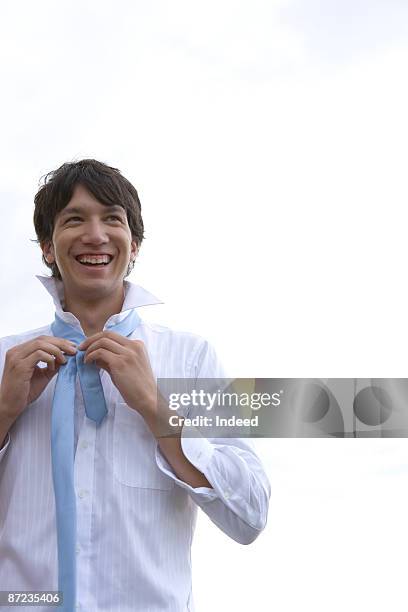 young man adjusting tie, smiling - hawaii hemd stock-fotos und bilder