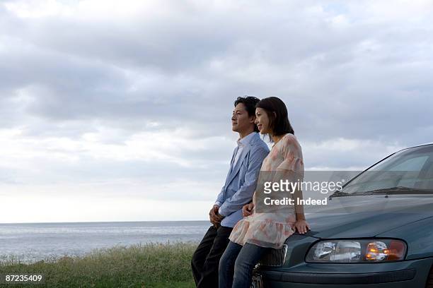 couple leaning on car, looking at view - man leaning on car stock-fotos und bilder