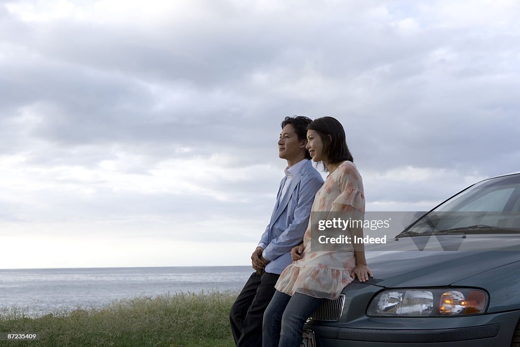 Couple leaning on car, looking at view