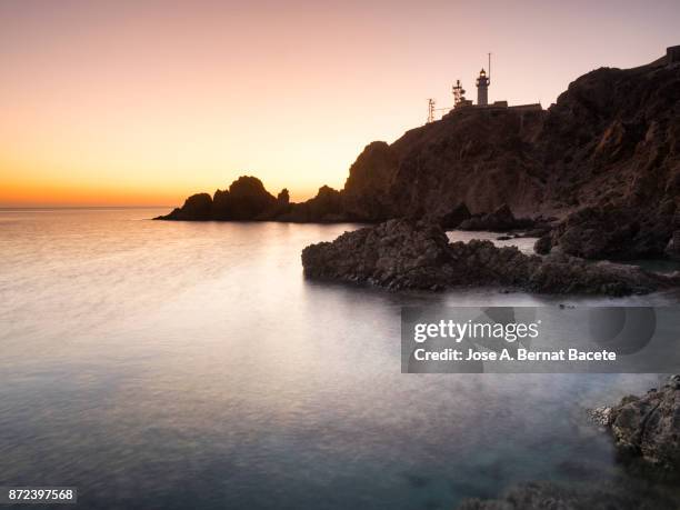 sunset on the beach and rocky coast with the silhouette of big cliffs and a 	lighthouse . cabo de gata - nijar natural park, sirens reef, biosphere reserve, almeria,  andalusia, spain - lighthouse reef stock pictures, royalty-free photos & images