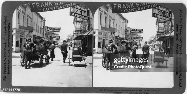 Stereograph shows a trio men as they move a wagon of beer barrels along Coney Island's Ocean Avenue, New York, New York, 1904. They are approaching...